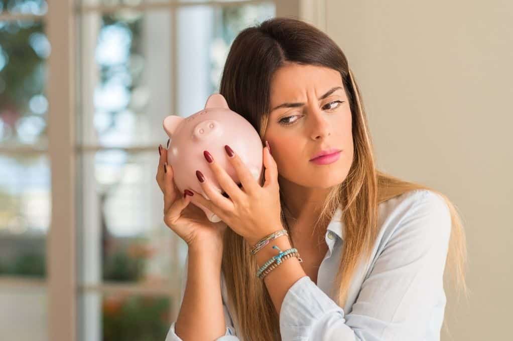 Women holding a piggy bank up to her ear with an inquisitive face, wondering what 42000 A Year Is How Much An Hour?