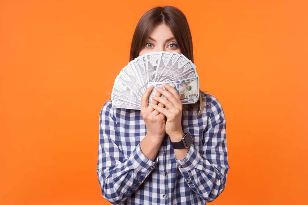 woman holding up hands of money hiding her face